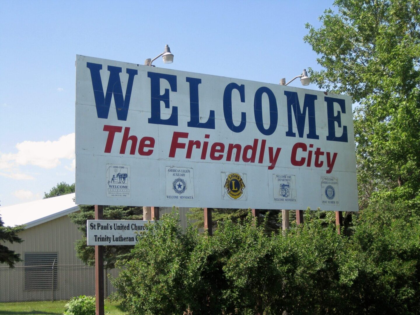 A welcome sign in front of trees and bushes.